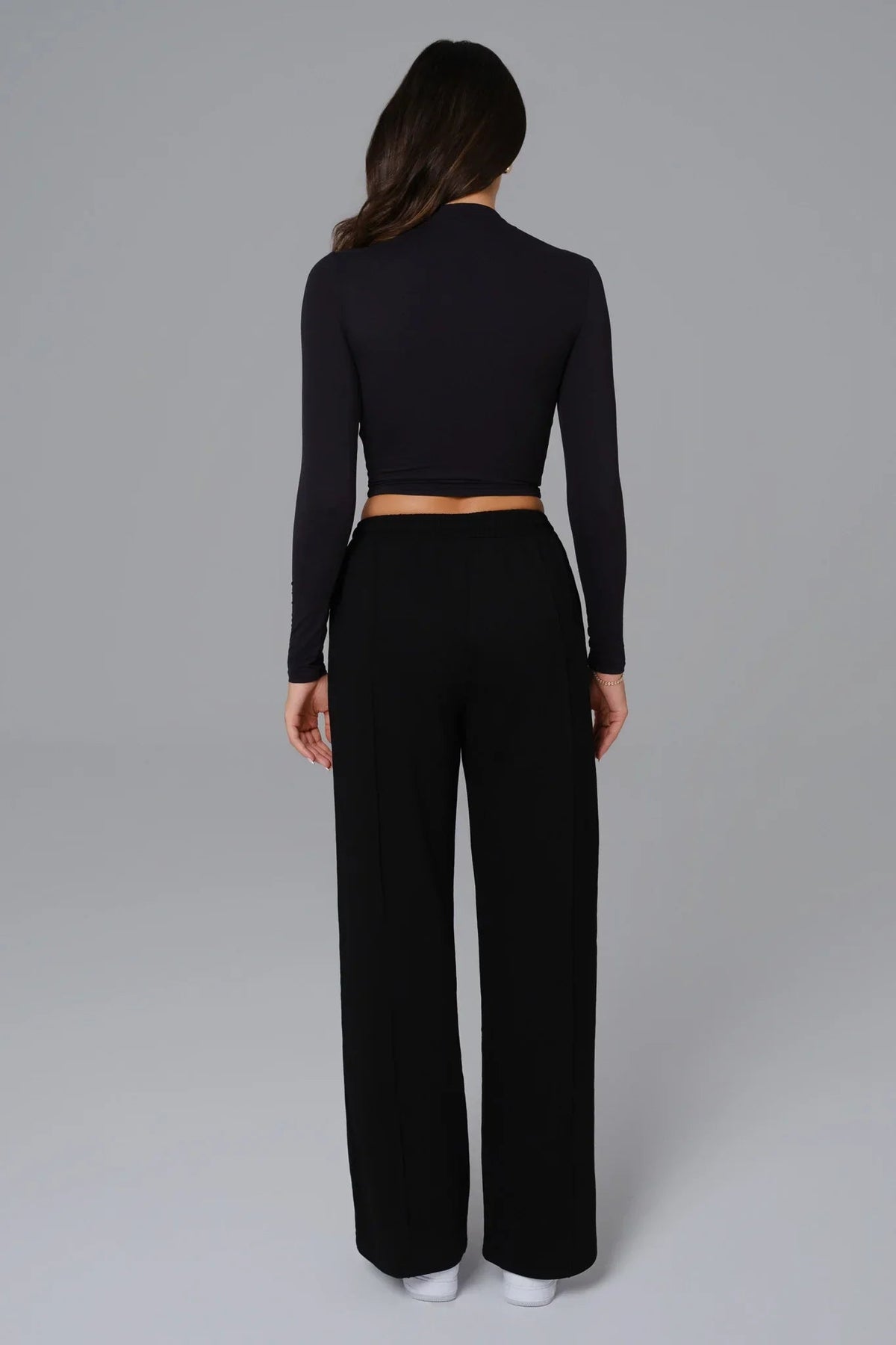 Person wearing a black long-sleeve top and wide-leg pants on a gray background