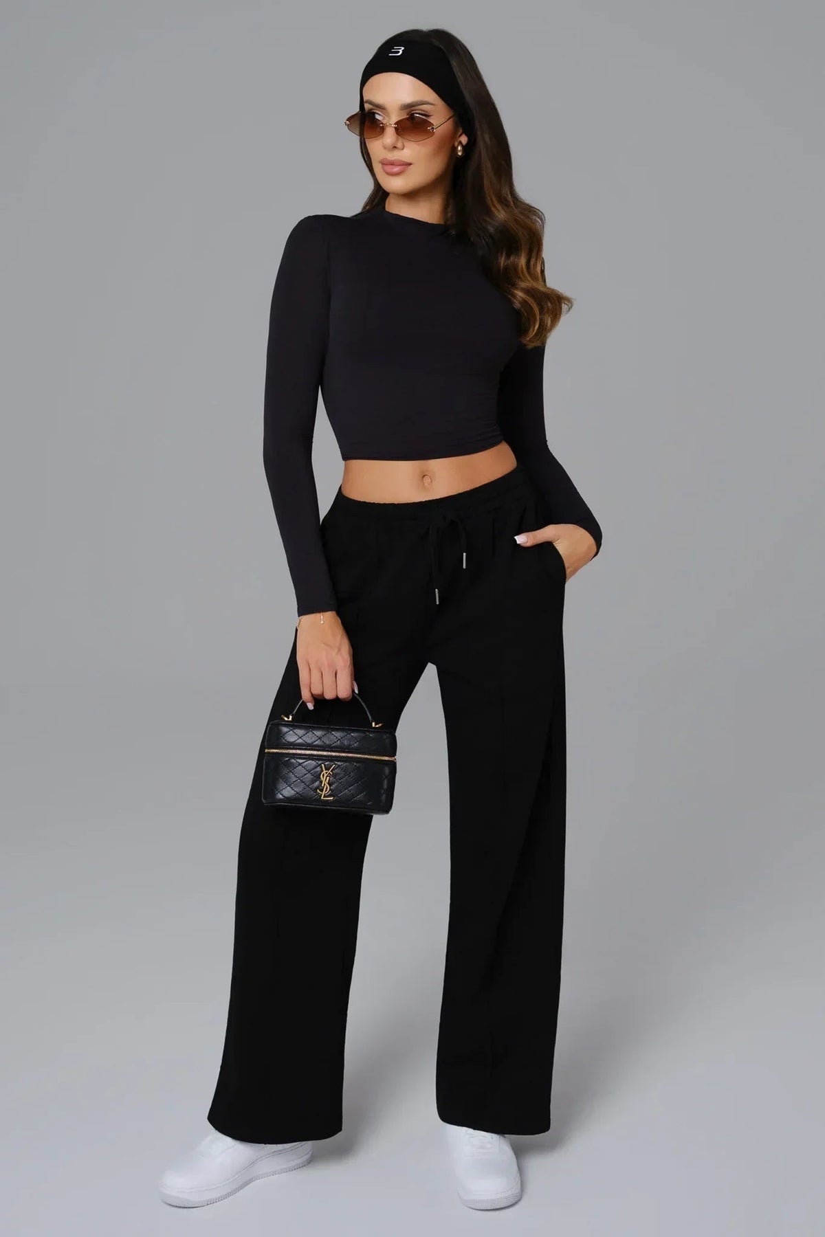 Woman wearing a black outfit with a handbag on a gray background
