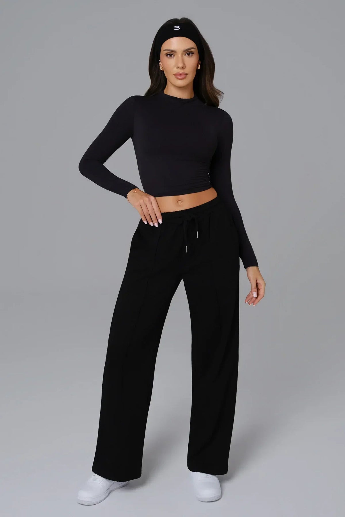 Woman wearing a black long-sleeve top and black pants on a gray background