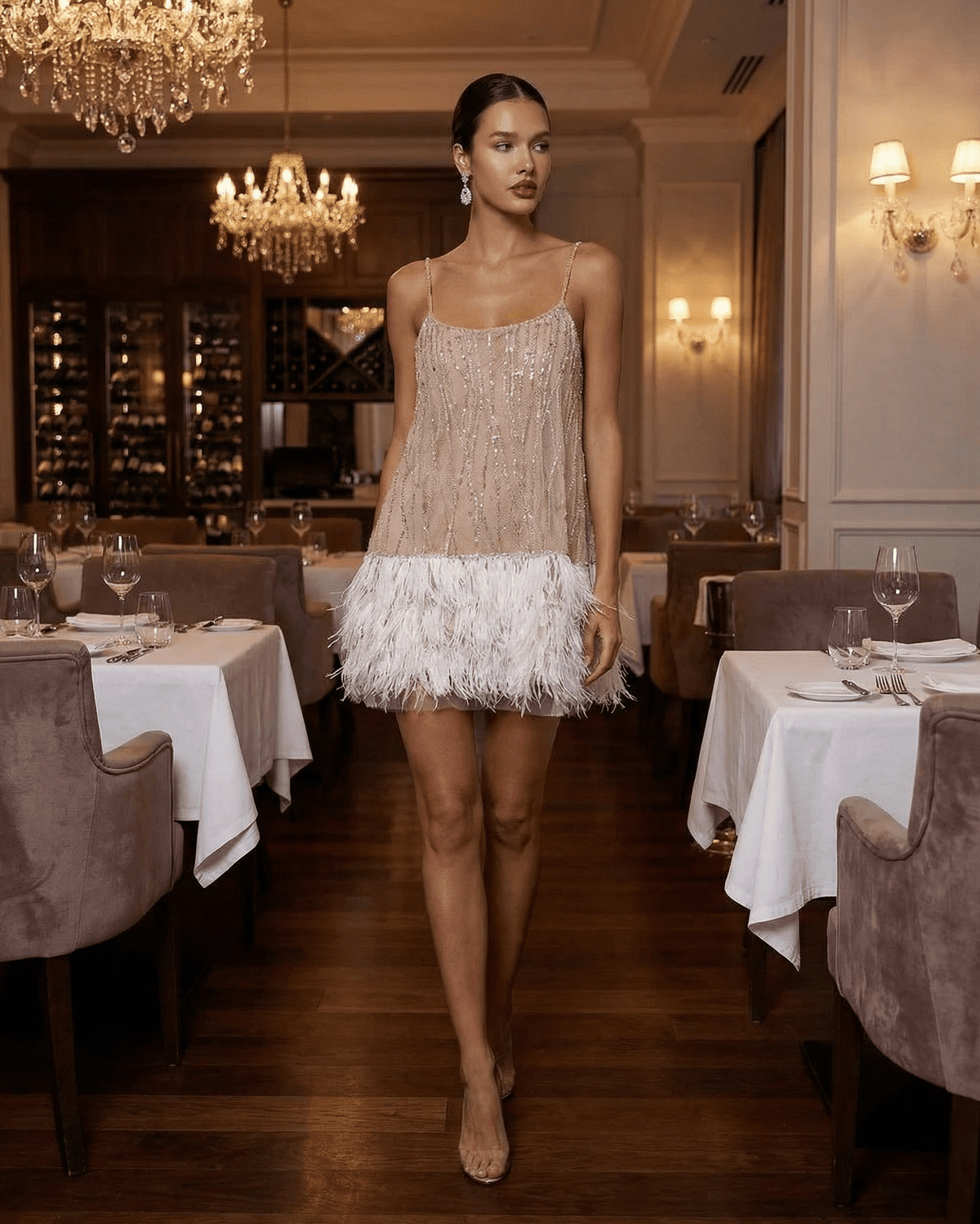 Celeste Mini Dress by Lauven, a sequin tulle fairycore mini dress with feather tassel hem in an elegant restaurant setting.