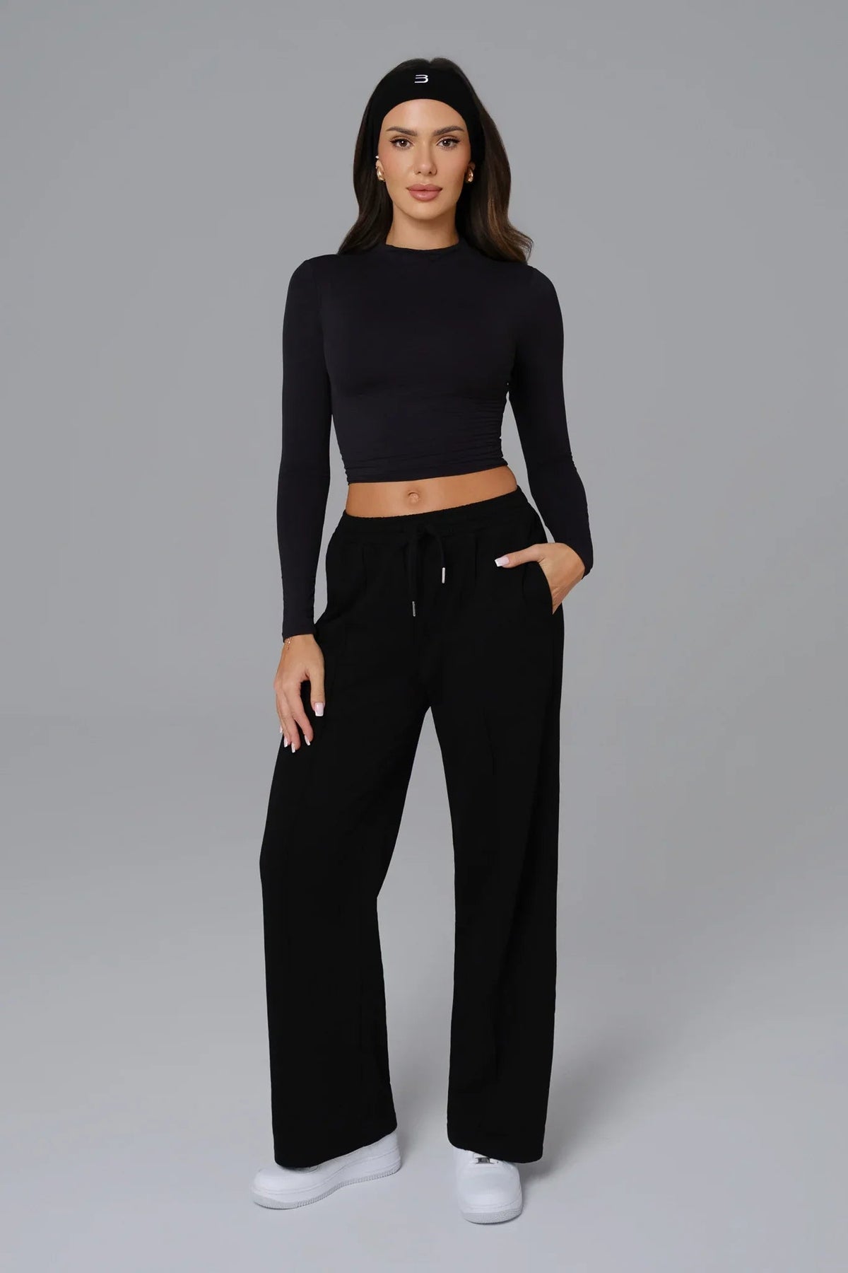 Woman wearing a black outfit with a crop top and wide-leg pants on a gray background